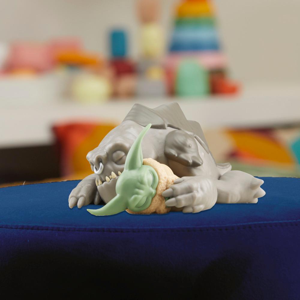 Grogu nestled beside the sleeping Rancor figure on a blue ottoman, manufacturer view of the Taming the Beast Pack