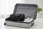 Black folding travel duffel bag placed inside open hardside suitcase showing extra packing space
