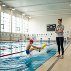 Youth swim coach watching a young swimmer practice kick drills with fins at an indoor competition pool