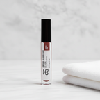 Arbonne Glossed Over Lip Gloss in Anise 0.1 fl oz on a white vanity beside a plain towel