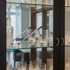 Undici swizzle stick chiller in organized glass barware cabinet next to elegant crystal tumblers