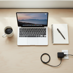 Flat-lay of a clean home office desk with open laptop, notebook, coffee mug, and slim black power adapter plugged into wall