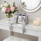 Lifestyle image - silver makeup organizer case as gift with satin ribbon flowers and candles on white vanity, gifting scene for visual context only