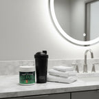 Dan's Magic Morning Elixir tub on modern bathroom vanity with blender bottle and white towels for wellness preparation