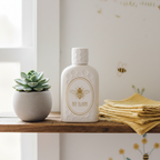 Lifestyle — cologne bottle with bee-themed label on wooden nursery shelf beside small succulent and folded yellow muslin cloth, soft natural light — editorial for visual context only