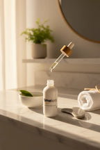 Healthy morning skincare routine with a white dropper bottle of pure face oil in soft golden morning sunlight on white marble vanity