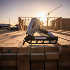 Pneumatic framing nailer laying across stacked dimension lumber at sunrise on a job site