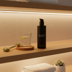 Revision Skincare Vitamin K Serum pump bottle next to jade roller and glass of water on light oak counter – post-procedure recovery display