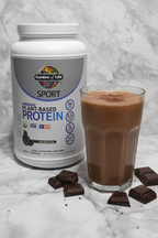 Garden of Life Sport Organic Plant Protein tub beside chocolate protein shake with cocoa powder on marble surface