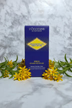 Minimalist display of botanical face serum surrounded by fresh yellow wildflowers and green leaves on white marble