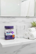 Natrol Sleep+ Calm Gummies jar on white marble vanity with glass of water, towels and succulent — More4less Outlet