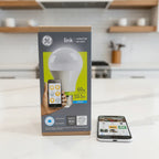 GE Link A19 Connected LED Bulb box on white quartz kitchen island next to smartphone displaying smart home app interface