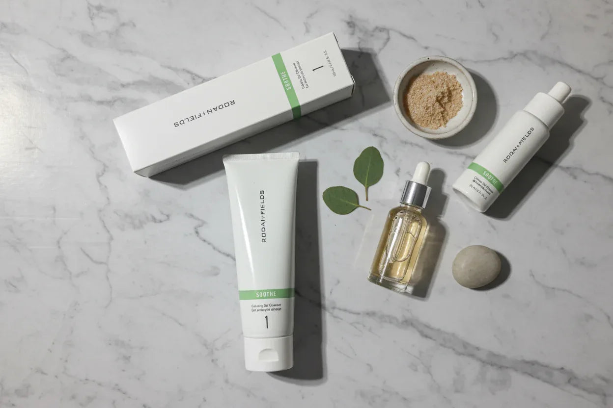 Flat lay of Rodan + Fields SOOTHE Calming Gel Cleanser tube and box alongside neutral skincare palette on marble