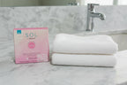 SOL by Jergens pink tanning towelettes box on marble bathroom counter beside white face towel