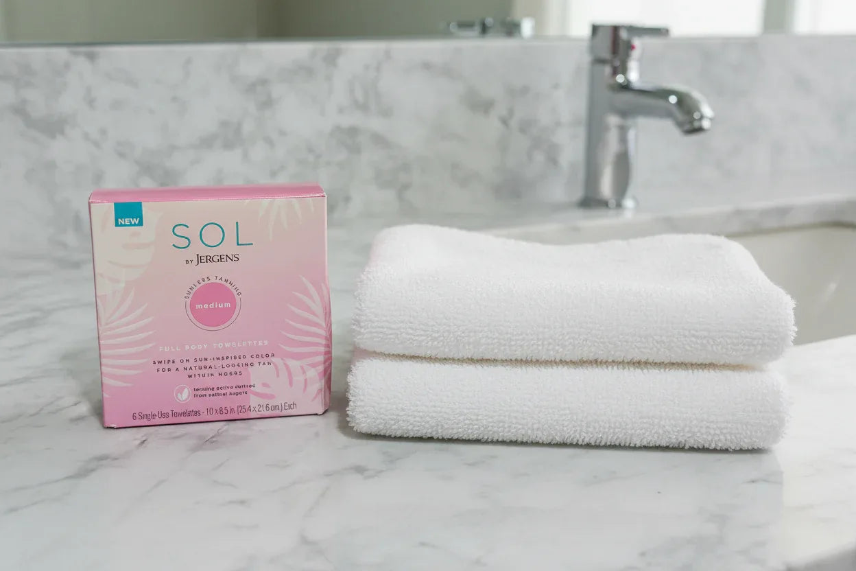 SOL by Jergens pink tanning towelettes box on marble bathroom counter beside white face towel