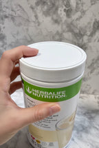 Close-up in-hand shot of Herbalife Formula 1 French Vanilla canister lid and label detail on white marble