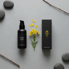 Minimalist flat-lay of Revision Skincare Vitamin K Serum bottle and black box with yellow arnica flower on gray concrete surface