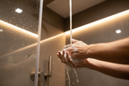 Close-up of hands creating rich lather under warm running water in modern glass shower
