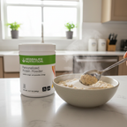 White Herbalife Nutrition Personalized Protein Powder tub next to a bowl of oatmeal with a tablespoon of white protein powder being stirred in, bright morning kitchen setting.