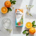 Floradix Calcium Magnesium supplement box flat lay on white marble with oranges and chamomile flowers