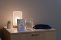 Winged Wellness Sleepyhead gummies box on nightstand with glass of water and silk sleep mask