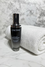 Elegant dark glass serum dropper bottle beside a folded white spa towel on white marble
