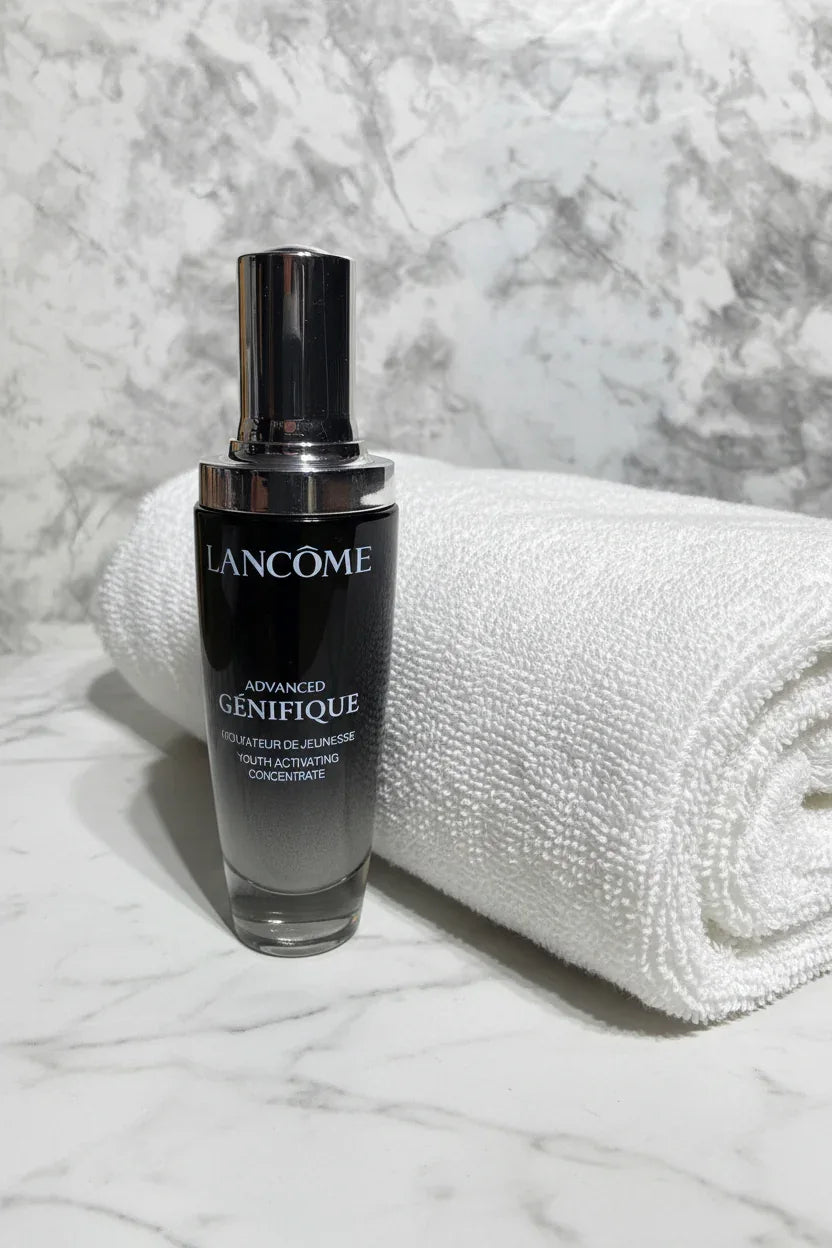 Elegant dark glass serum dropper bottle beside a folded white spa towel on white marble