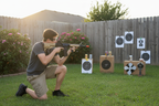 Person aiming Game Face Elite Renegade airsoft rifle at backyard targets — spring-powered military-style rifle with adjustable stock and tan handguard