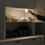 Person reaching into a dark kitchen cabinet illuminated by a tap-activated puck light mounted inside
