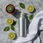 Sustainability-themed self-care flat lay with silver aluminum bottle, bergamot slices, basil leaves, and small cactus on marble