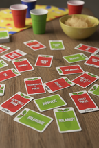 Close-up flat lay of Apples to Apples red and green playing cards spread on wooden table — More4less Outlet