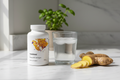 Thorne supplement bottle on marble surface next to glass of water, ginger root, and small green plant