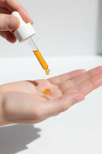 Hand dispensing a single drop of amber facial serum onto a smooth clean palm in soft natural lighting