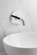 Grohe Lineare New StarLight chrome wall-mount lavatory faucet trim installed on white marble wall above modern vessel sink with water dripping