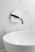 Grohe Lineare New StarLight chrome wall-mount lavatory faucet trim installed on white marble wall above modern vessel sink with water dripping