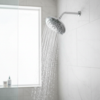 Pfister Arterra polished chrome shower head mounted on a white marble tile shower wall with water streaming.