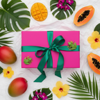 Lifestyle image — bright pink perfume box on white tissue paper with green ribbon bow, vibrant tropical gifting flatlay for visual context only