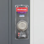 Kwikset satin nickel door knob against sleek gray and white wood panel door backdrop.