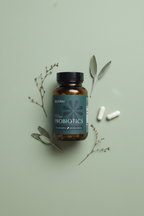 BIOMA Probiotics amber glass bottle flat lay on sage green background with two capsules and botanical leaves