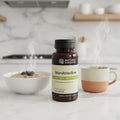 Nature's Sunshine Marshmallow Root bottle on modern white quartz kitchen counter beside white ceramic bowl of oatmeal and warm cup of herbal tea