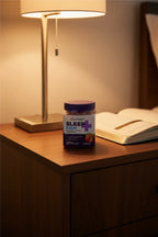 Natrol Sleep+ Calm Gummies jar on dark walnut nightstand with reading lamp and wellness journal — More4less Outlet