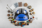 Maxx Explore Rock Tumbler flat lay on grey background with polished gemstones grit bags rough rocks and jewelry pieces