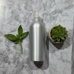 Silver aluminum lotion pump bottle on white marble beside a small green succulent and fresh basil sprig
