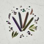 Flat lay of jewel-tone mechanical eyeliner pencils on white marble with gemstones