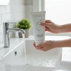 Woman holding ZO Skin Health Exfoliating Cleanser 200mL tube over a white bathroom sink during a morning skincare routine