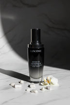 High-end cosmetic display featuring a dark glass luxury serum bottle with soft shadows and silver cap on white marble