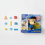 PAW Patrol Room Patrol Chase Interactive Plush Toy (12-inch) — Chase plush in blue police uniform flat-lay on white surface alongside original retail display box with colorful PAW Patrol accessories scattered around — bright playful toy flat-lay