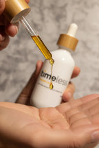 Glass pipette releasing a golden drop of pure argan oil into clean cupped palms in soft warm natural lighting