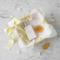 Lifestyle — pastel yellow gift basket flatlay with cologne bottle, honeycomb soap, yellow ribbon bow, and white tissue paper on marble — editorial for visual context only