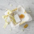 Lifestyle — pastel yellow gift basket flatlay with cologne bottle, honeycomb soap, yellow ribbon bow, and white tissue paper on marble — editorial for visual context only